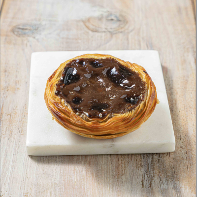 Pastelaria com massa folhada e recheio castanho com frutos pretos sobre placa de mármore