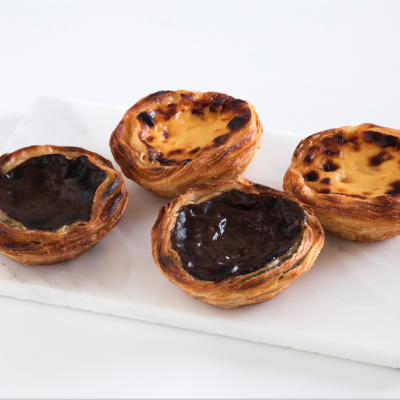 Quatro pastéis de nata, dois de creme amarelo e dois com chocolate, numa base branca de mármore