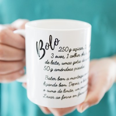 Caneca branca com receita impressa em português a ser segurada por uma pessoa com camisola azul-turquesa