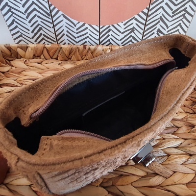 Mala castanha em camurça aberta com fecho metálico sobre superfície de palha