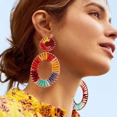 Brincos grandes coloridos em forma de argola usados por mulher com blusa amarela estampada