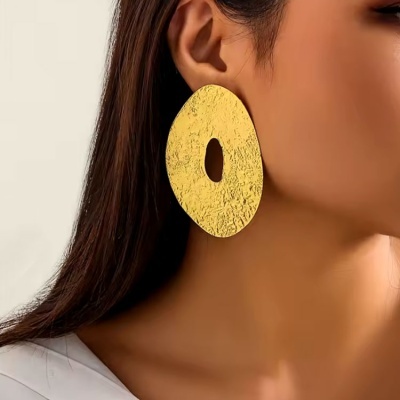 Brinco dourado grande com textura martelada, usado por pessoa