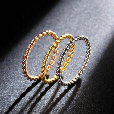 Três anéis finos torcidos em dourado, prata e cobre sobre superfície preta