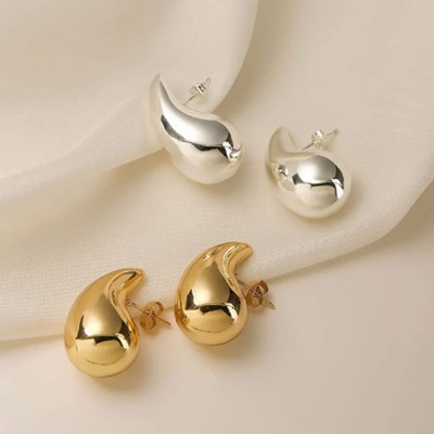 Dois pares de brincos curvos, um prateado e outro dourado, sobre tecido branco