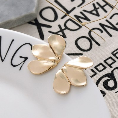 Brincos dourados em forma de pétalas sobre prato branco e pano com texto.