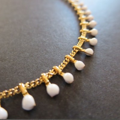 Colar dourado com pendentes brancos em fundo preto fosco