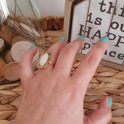 Mão com anel dourado e verniz azul sobre superfície de palha com quadro decorativo ao fundo