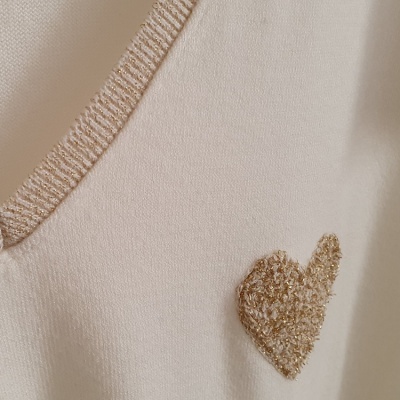 Detalhe de blusa creme com coração dourado bordado
