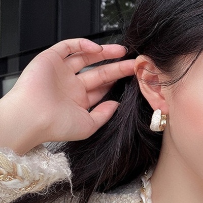 Brinco dourado com detalhe branco visível na orelha de mulher com cabelo escuro.