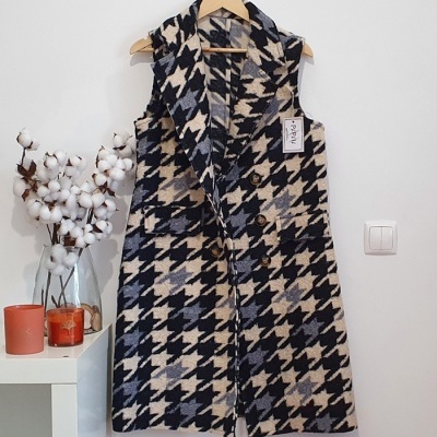 Colete feminino padrão pied-de-poule em preto, cinzento e bege pendurado num cabide de madeira.