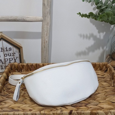 Bolsa tipo pochete branca com fecho dourado sobre superfície de madeira trançada