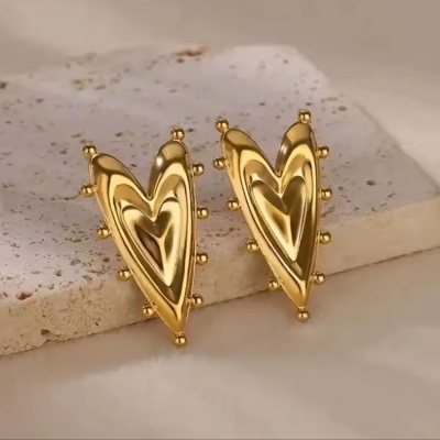 Brincos dourados em forma de coração com esferas nas bordas sobre pedra clara