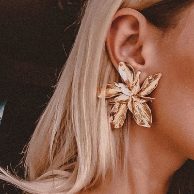 Brinco grande em forma de flor dourada com textura metálica na orelha de uma pessoa