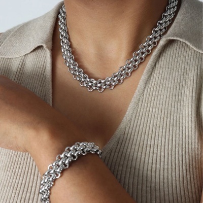 Colar e pulseira prateada de corrente grossa em pessoa com camisa bege canelada