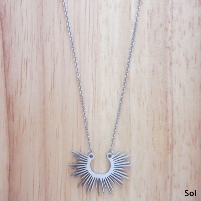 Colar prateado com pendente em forma de sol sobre madeira clara