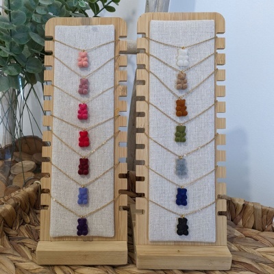 Colares com pendentes em forma de ursinho coloridos exibidos em suportes de madeira com tecido bege