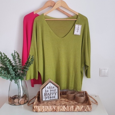 Dois casacos de malha verde e rosa pendurados e elementos decorativos numa mesa branca