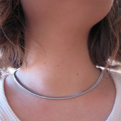Colar tipo gargantilha em metal prateado texturizado numa pessoa com cabelo castanho e roupa branca
