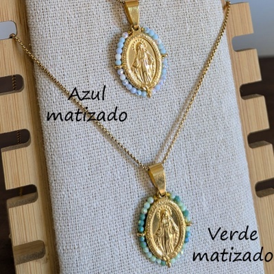 Colares dourados com medalhas religiosas ovais adornadas com contas azuis e verdes sobre almofada clara