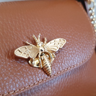Fecho em forma de inseto dourado numa bolsa castanha de pele sintética