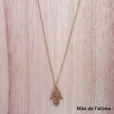 Colar dourado com pendente Mão de Fátima sobre fundo de madeira