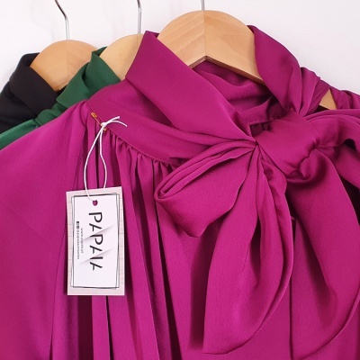 Blusas coloridas com gola de laço penduradas em cabides de madeira