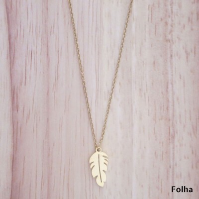 Colar dourado com pendente em forma de folha sobre fundo de madeira clara