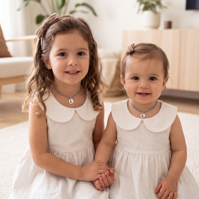 Duas crianças com vestidos brancos e acessórios de cabelo castanhos em ambiente interior