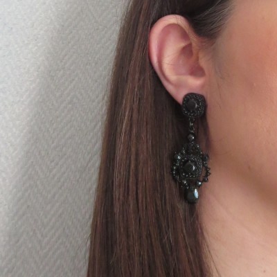 Brinco pendente preto com detalhes arredondados numa orelha