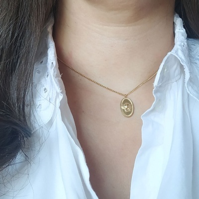 Colar dourado com pendente oval usado com camisa branca bordada