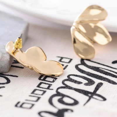 Brincos dourados em forma de flor sobre tecido com texto preto