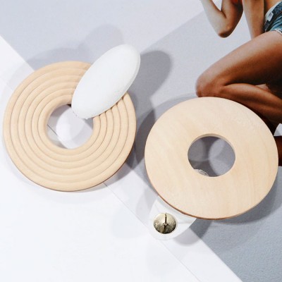 Dois objetos circulares de madeira clara num fundo cinzento claro e branco, com uma perna humana ao lado