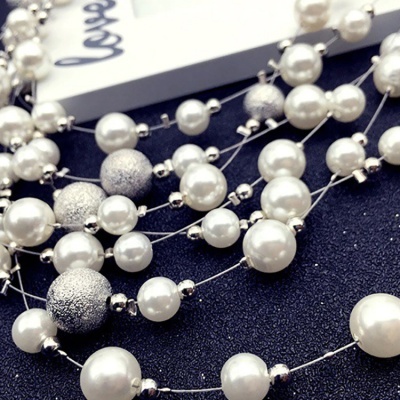 Colar de pérolas brancas e esferas prateadas sobre superfície preta com cartão branco 'love'