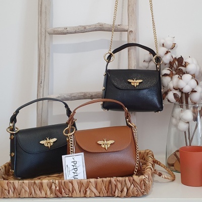 Três malas pequenas em couro sintético com detalhes de abelha dourada expostas num tabuleiro de vime