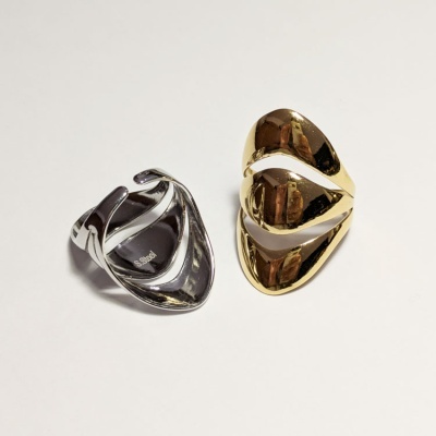 Dois anéis metálicos, um prateado com texto 'S.Steel' e um dourado entrelaçado, sobre fundo branco