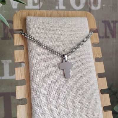 Colar prateado com pendente de cruz sobre suporte de madeira e tecido bege