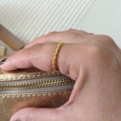 Anel dourado de espiral num dedo apoiado em superfície bege com fecho de correr