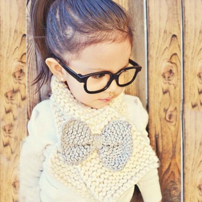 Cachecol tricotado bege com laço cinza em criança com óculos em fundo de madeira.