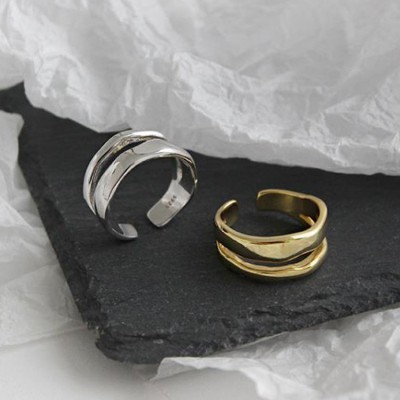Dois anéis abertos, um prateado e outro dourado, sobre ardósia preta e papel branco amassado