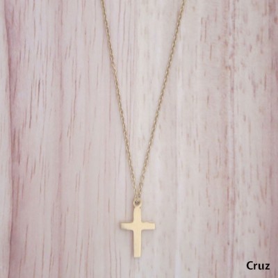 Colar dourado com pendente em cruz sobre fundo de madeira clara