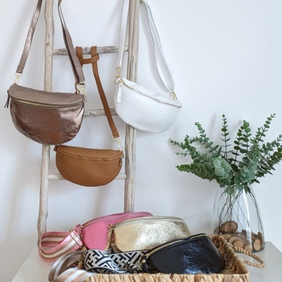 Bolsas tiracolo coloridas penduradas numa escada e numa cesta junto a um vaso com plantas