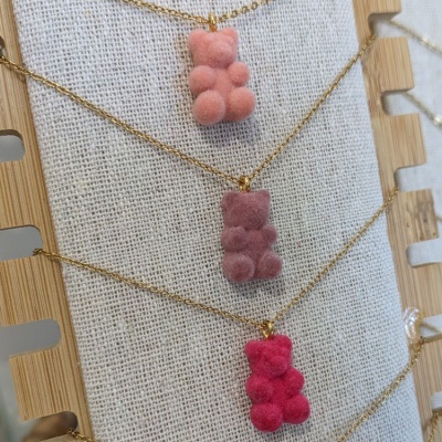 Colares com pendentes em forma de gomas ursinhos em tons de rosa e vermelho sobre fundo de tecido bege