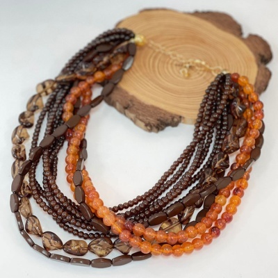 Colar com múltiplas voltas em tons castanhos e laranja sobre base de madeira