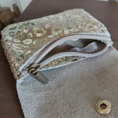 Bolsa pequena cinza claro com padrão dourado e fecho de correr branco aberta sobre superfície de madeira