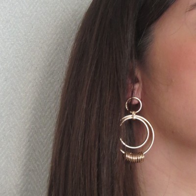 Brincos dourados de argolas entrelaçadas em orelha