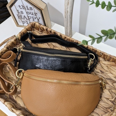 Duas bolsas tipo pochete, preta e castanha, numa cesta de palhinha com decoração ao fundo