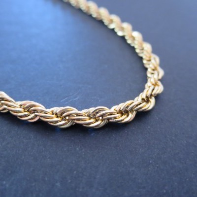 Colar dourado com elos entrelaçados sobre fundo azul escuro