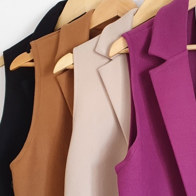 Quatro coletes sem mangas de cores diferentes pendurados em cabides de madeira.