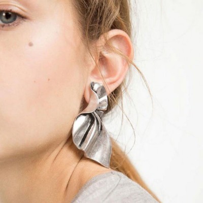 Brinco metálico prateado com design ondulado, usado por mulher