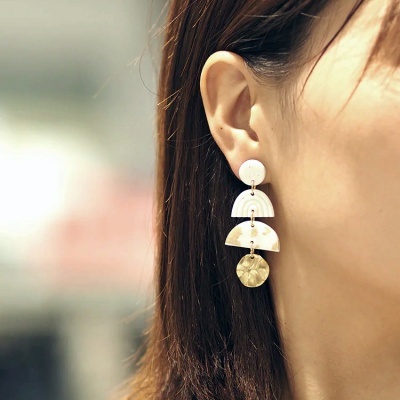 Brinco pendente creme e dourado numa orelha feminina